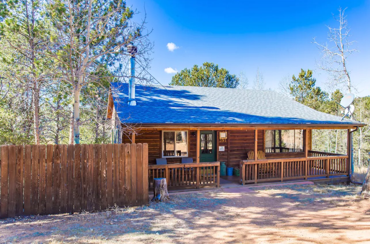 A quaint log cabin on a sunny day with a fenced in backyard