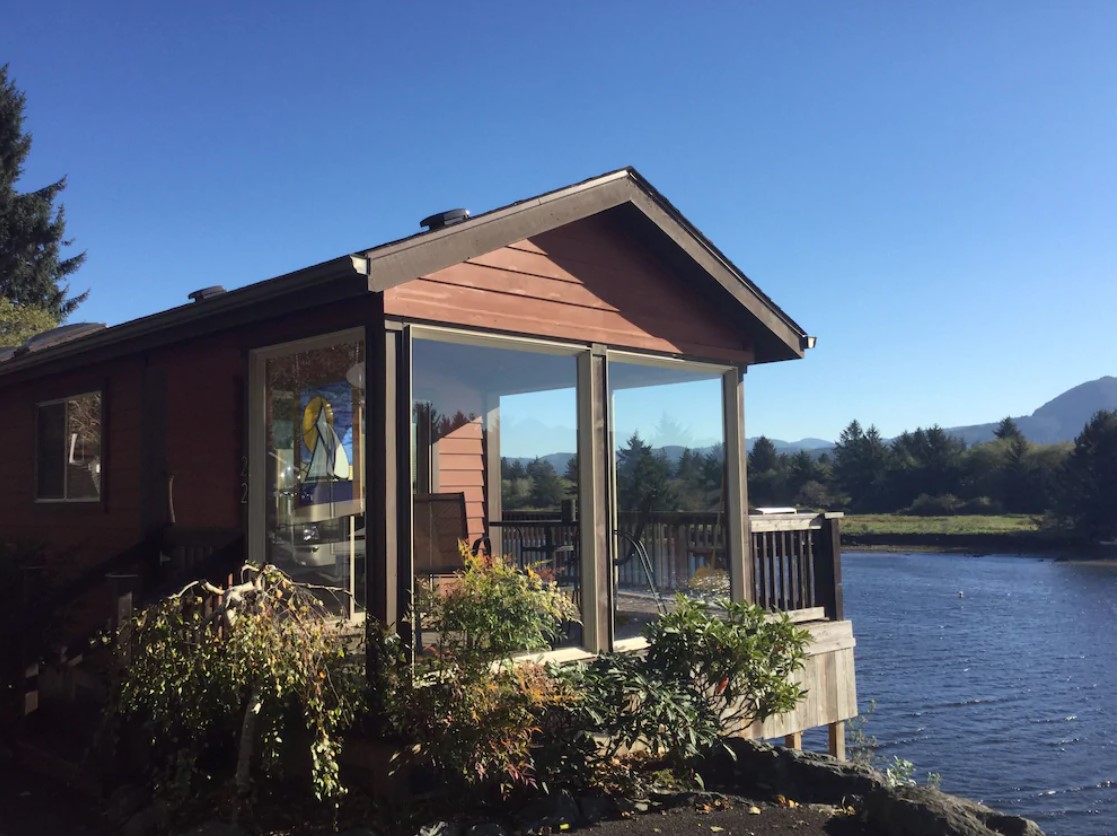 A cottage with a large sunroom and deck over looking a river in Oregon on a sunny day