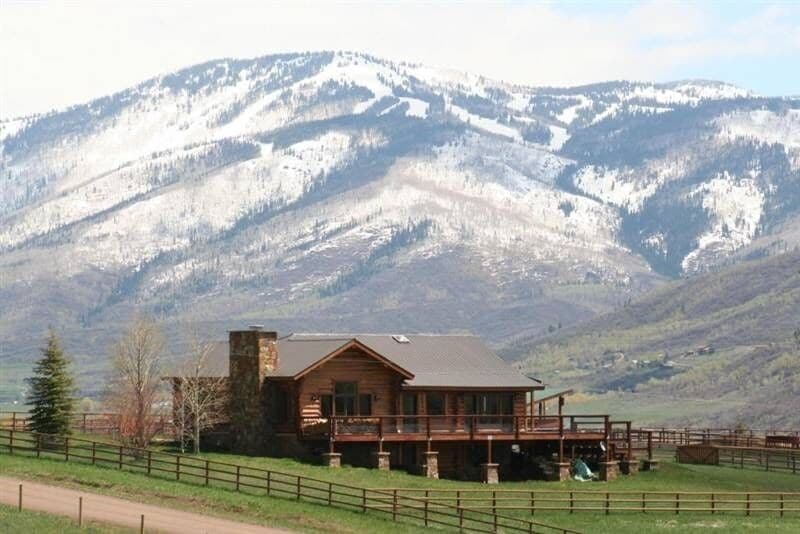 A large log home on a green field with the Rocky Mountains directly in the distance