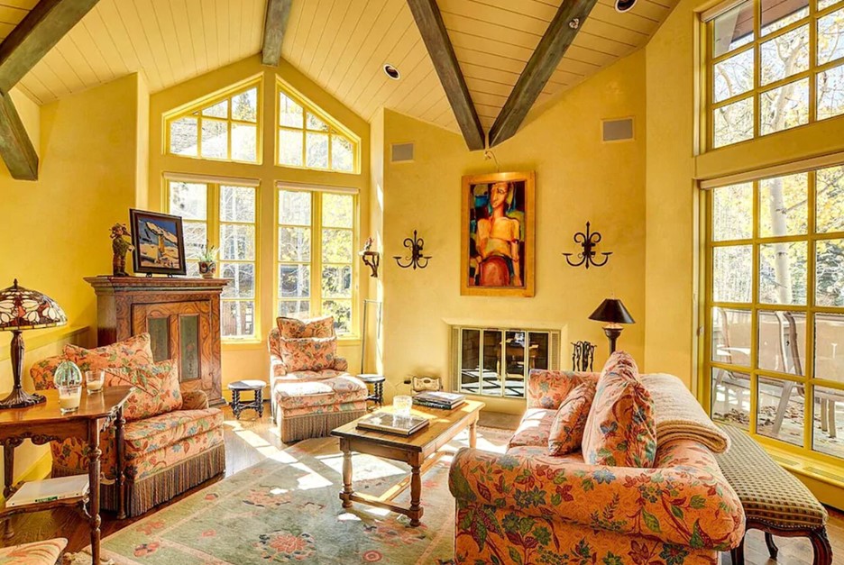 A living area painted a creamy yellow color with cozy furnishings and large windows letting the sun in