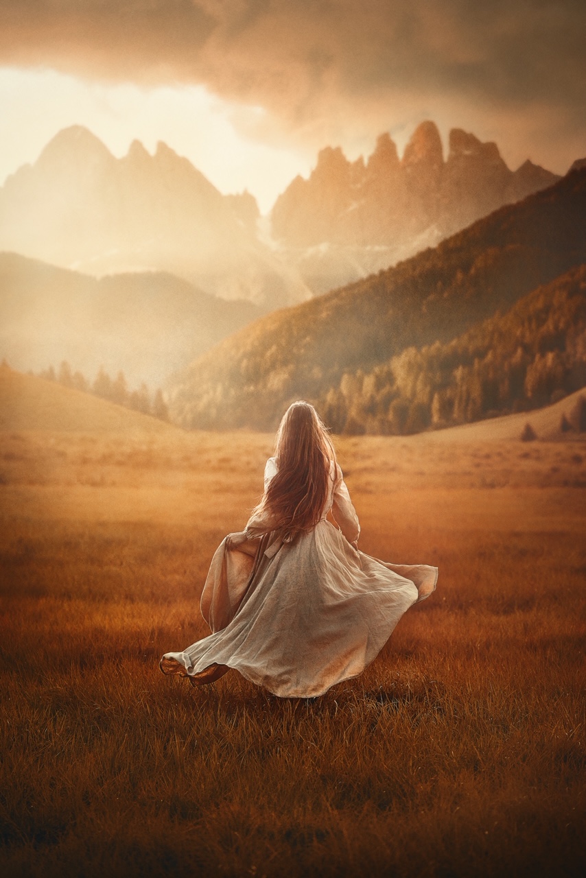 A woman standing in a field surrounded by mountains and trees wearing a linen dress