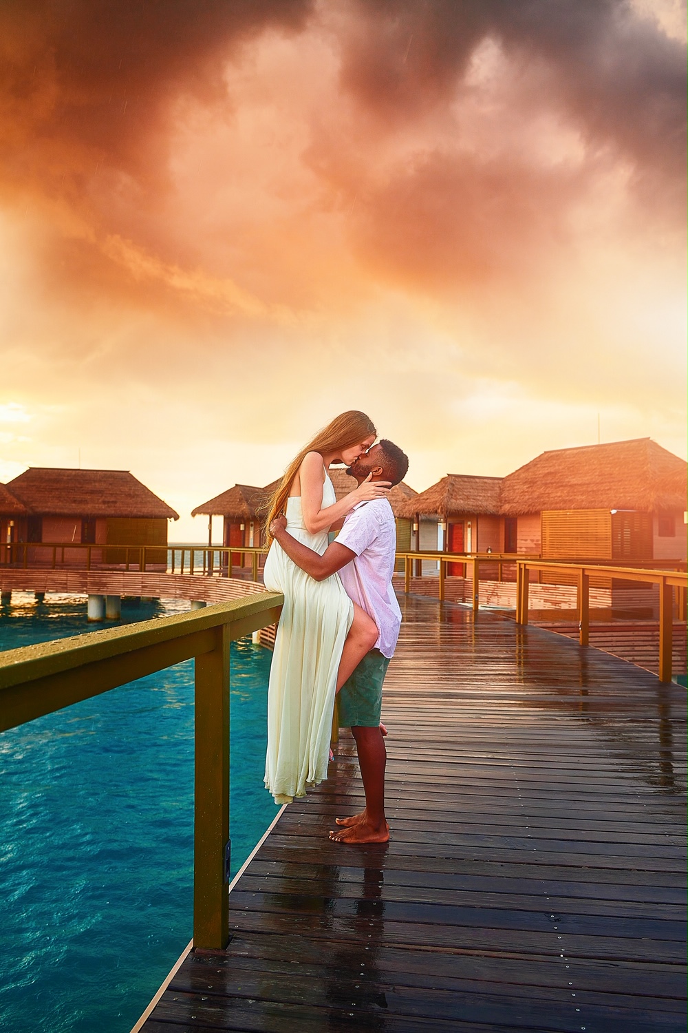 A couple kissing on a dock surrounded by overwater bungalows in Jamaica at sunset