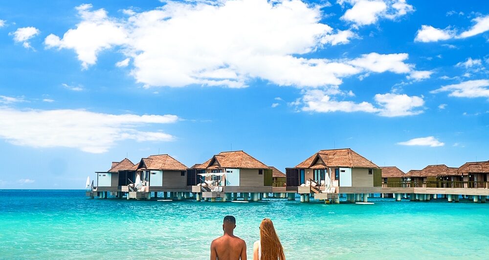 A couple standing in the ocean looking at overwater bungalows in Jamaica