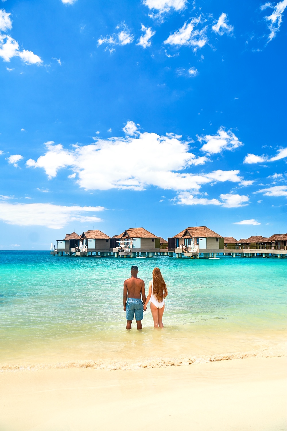 A couple standing in the ocean looking at overwater bungalows in Jamaica