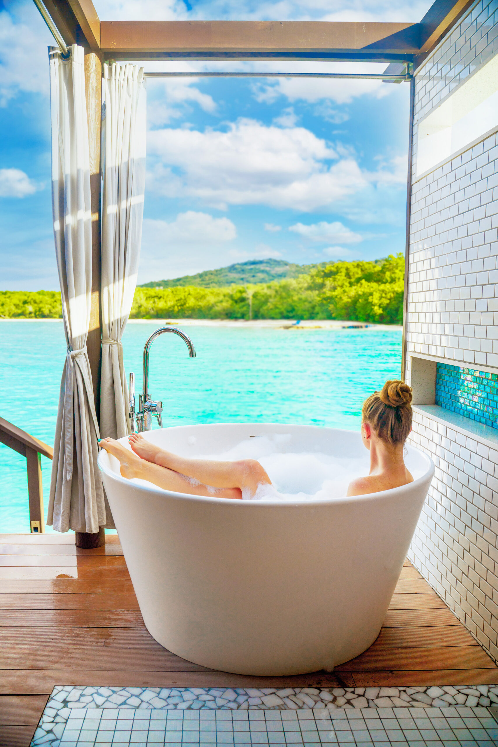 A woman sitting in an outdoor tub looking out at a view of the beach and mountains