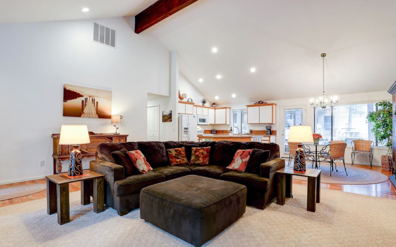 The large living area of one of the best vacation rentals in Oregon with a large brown sectional sofa, vaulted ceilings, a fully equipped kitchen, and a small dining area.