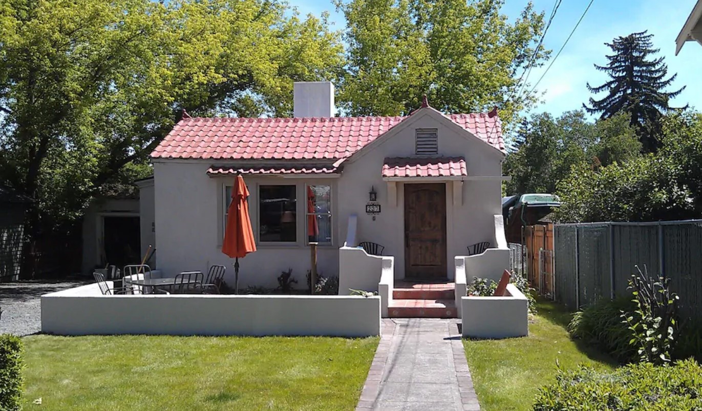 A cute historic bungalow with white stucco, a front courtyard, and a red shingled roof with a small yard in the front one of the best vacation rentals in Oregon