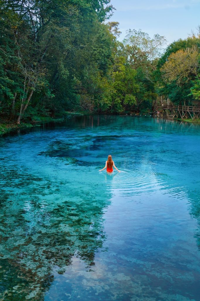 A woman in a red bathing suit with long hair standing in a crystal blue Florida spring.