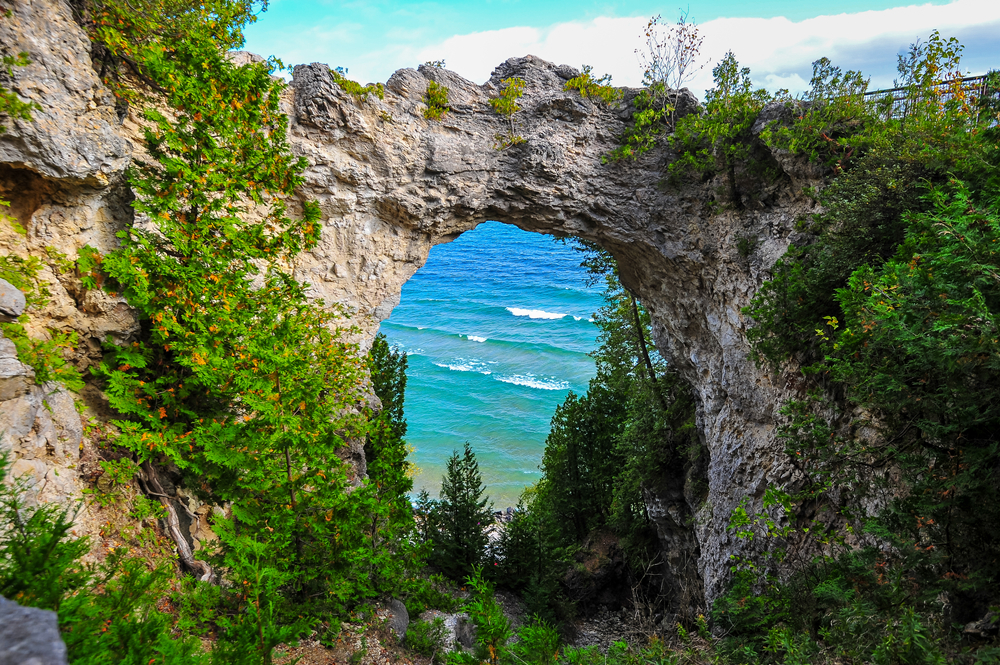 A natural stone arch on Mackinac Island Michigan with water in the background and surrounded by greenery