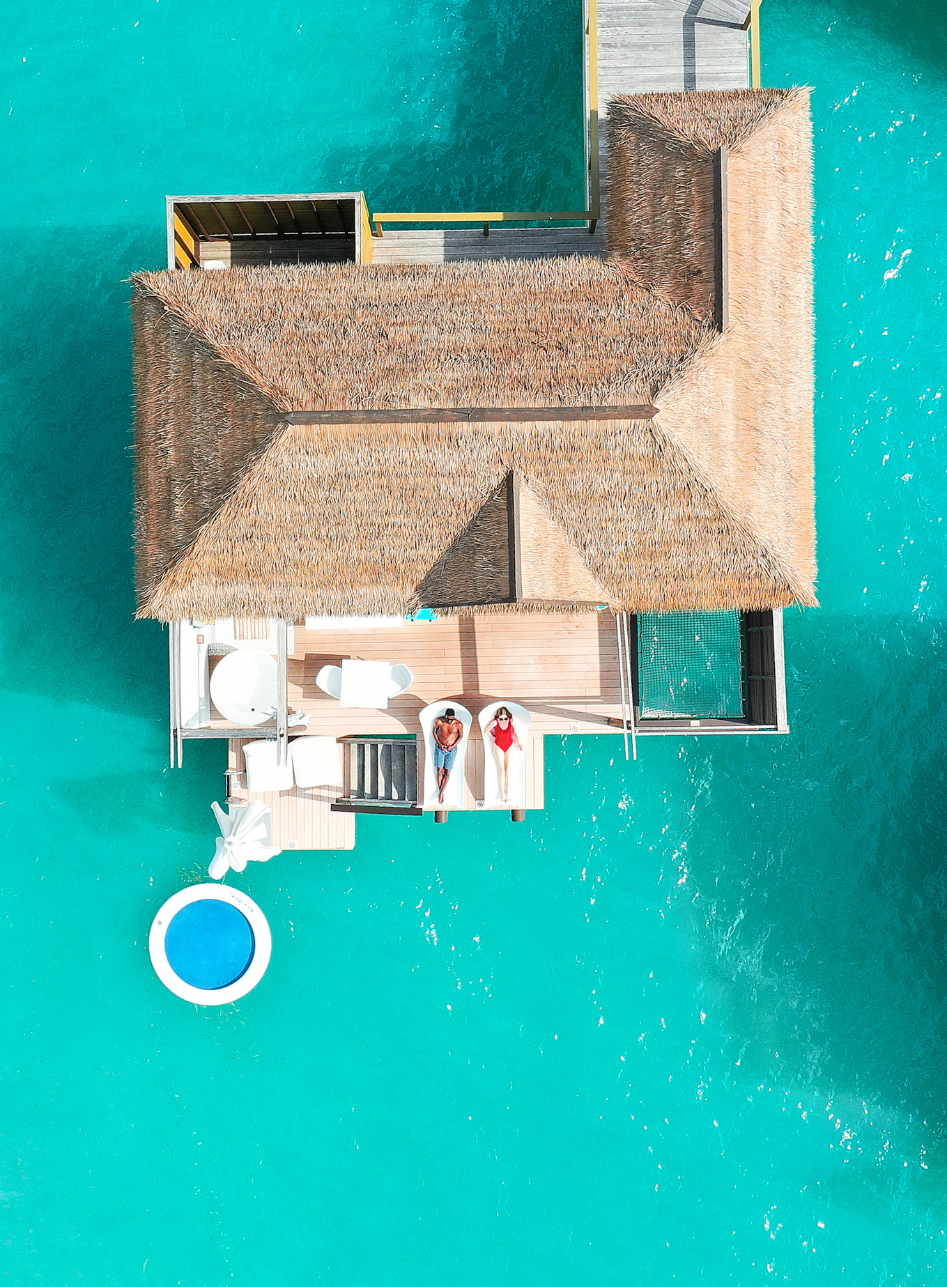 couple relaxing on deck of an overwater bungalows in jamaica in a red swimsuit with blue water