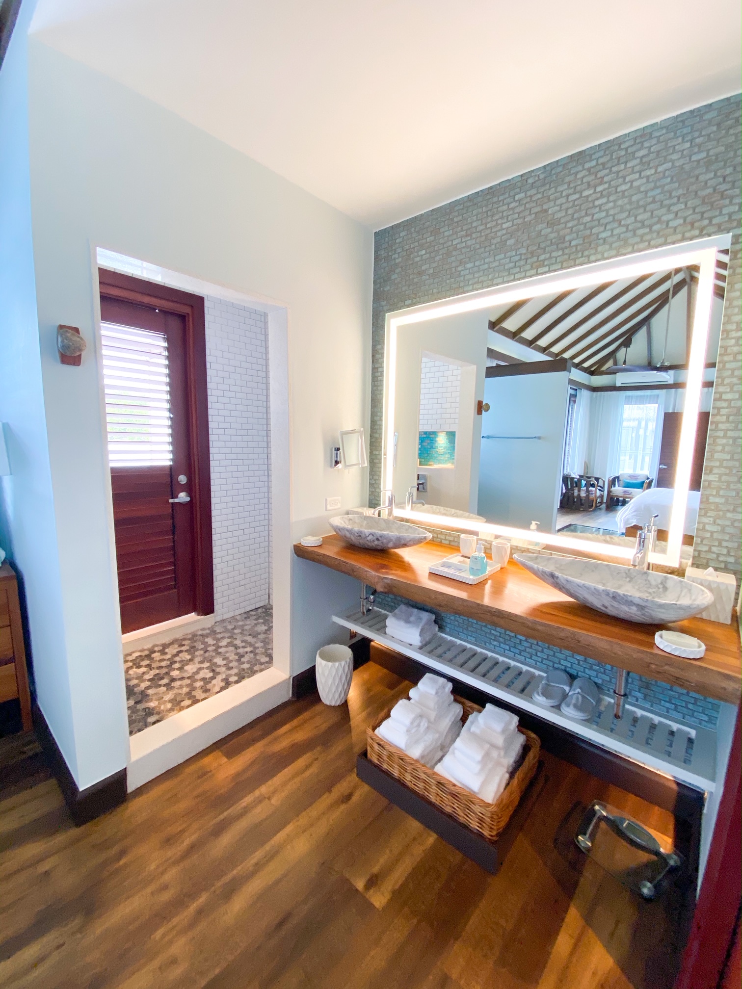 A luxury bathroom with a walk in shower, stone sinks, and a lit up mirror