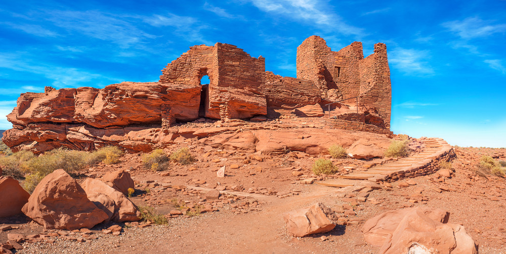 A historic pueblos at the Wupatki National Monument. They are ruins of what once was a house made of red sandstone bricks. It is a bright sunny day. 