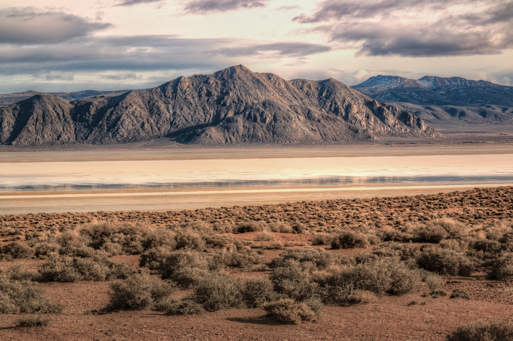 A view across the desert at the black mountains of the Black Rock Desert. It is a cloudy day and there is some small grass in the closest part of the desert.