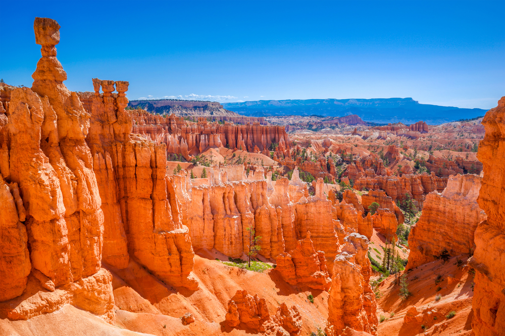 The large red sandstone rock formations looking down the valley of Bryce Canyon. In the distance you can see more red sandstone rock formations and mountains. One of the best Southwest road trip stops.