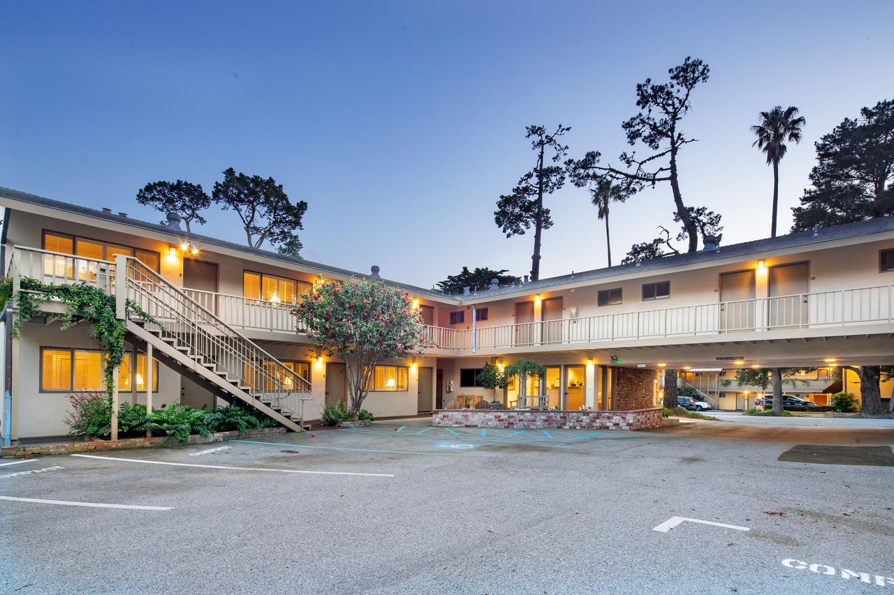 The exterior of a beach motel. The building is cream and fairly simple. It has two levels and plenty of rooms. Behind the building you can see large palm trees.