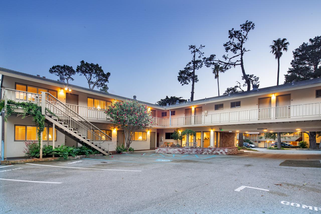 The exterior of a beach motel. The building is cream and fairly simple. It has two levels and plenty of rooms. Behind the building you can see large palm trees. 