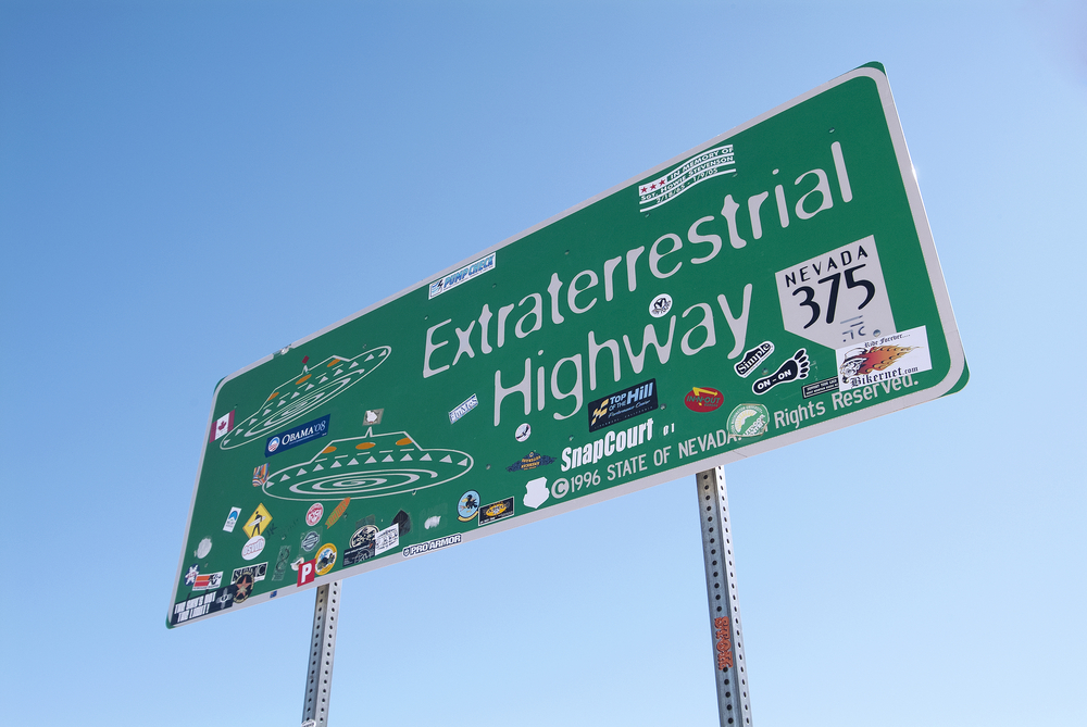 The highway sign for the Extraterrestrial Highway in Nevada. the sign uses the 'X-files' font and has UFOs on it. It has also been covered by stickers.