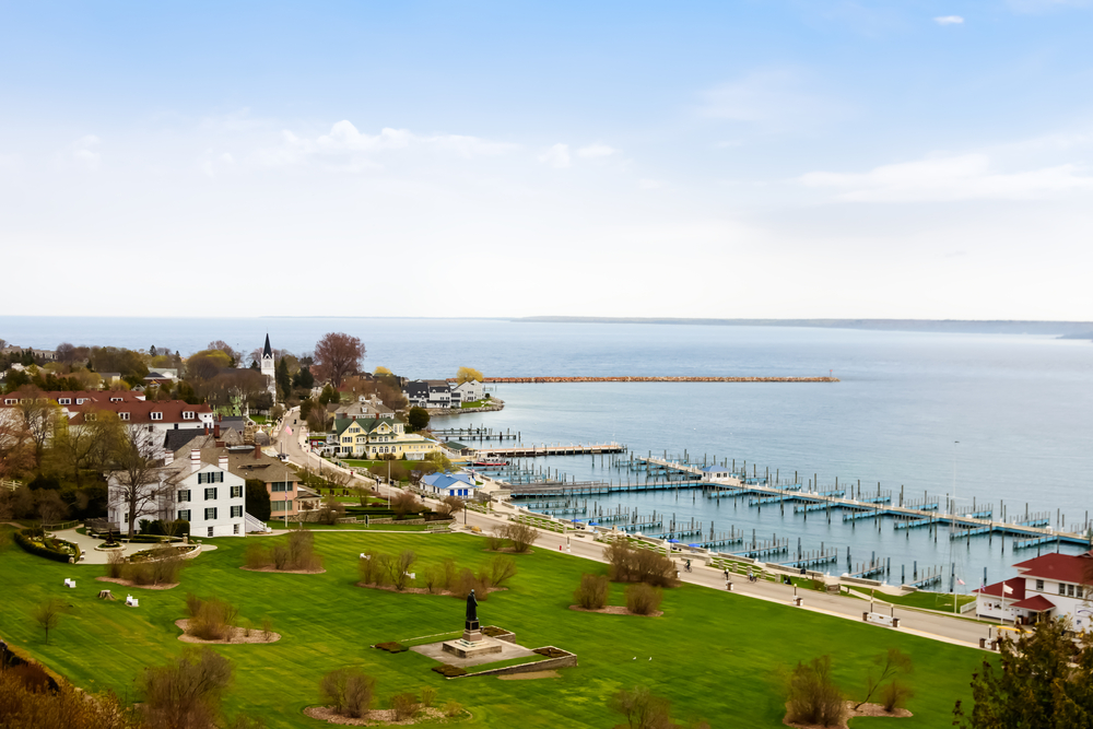 An aerial view of the harbor in Mackinac Island. You can see a green lawn, old buildings, and a large dock system but there are no boats in it.