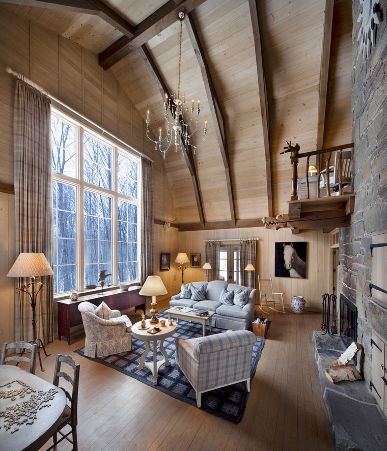 One of the cozy rooms at the Twin Farms resort in Vermont. It as a couch, two chairs, a fireplace, and lots of windows with tall ceilings and a chandelier hanging from the ceiling.