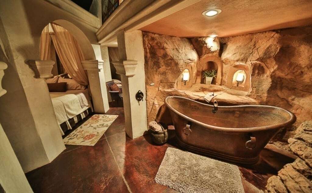 photo of the luxurious hammered metal bathtub in a bathroom styled with red desert rock walls and salt lamps