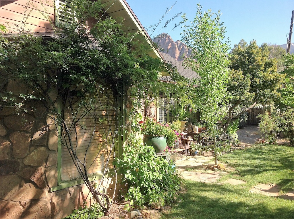 View of the lush garden exterior of the Historic Rose Cottage, one of the best Airbnbs in Utah. You can see the red rocks of Zion National Park behind the cottage.