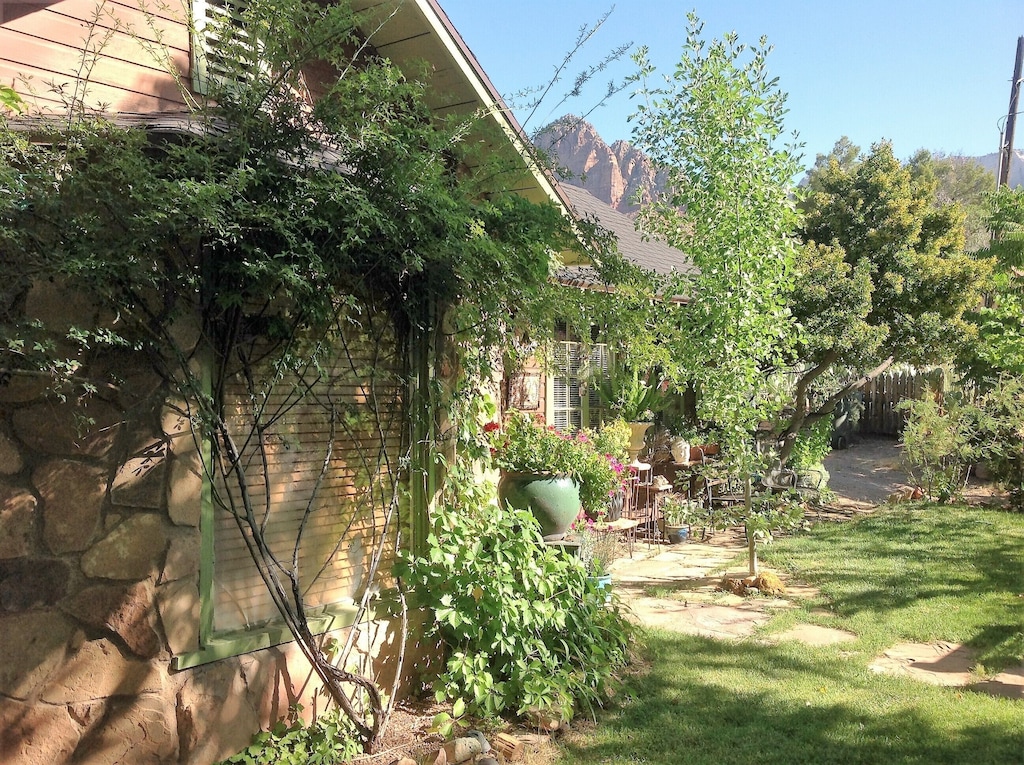 View of the lush garden exterior of the Historic Rose Cottage, one of the best Airbnbs in Utah. You can see the red rocks of Zion National Park behind the cottage. 