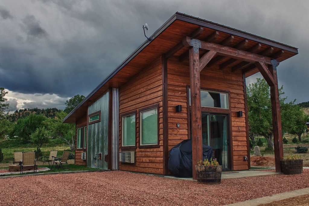 View of the cedar and sheet metal facade of the tiny home. Fire pit with 4 chairs and apple trees are visible. This is one of the best vacation rentals in Utah.