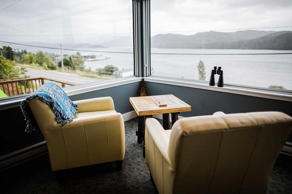 The interior of the lobby of the Bonne Bay Inn. There are two pale yellow leather chairs. The chairs are angled looking out two large windows. Out the windows you can see a bay landscape with hills in the distance. It is one of the best places to stay on a West Newfoundland itinerary. 