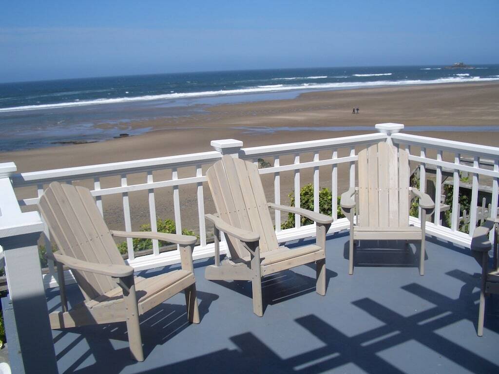 four cool retro deck chairs are in the foreground, the background is an expanse of sandy uncrowded beach, beautiful blue waters and blue skies. 