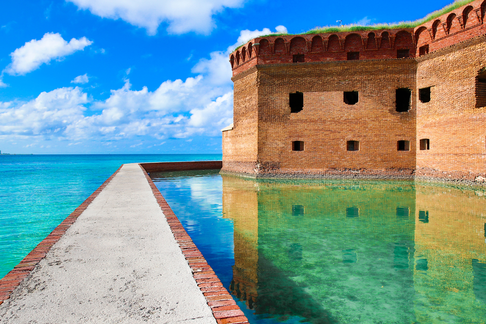 The historic fort in the water at Dry Tortugas National Park. The water is crystal blue and there is a pathway that separates the water from the fort. 
