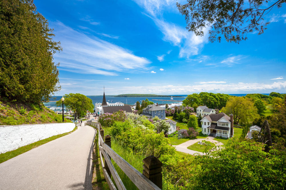 A view of Mackinac Island, one of the best islands in the USA. You can see Lake Huron in the distance and historic homes, buildings, and a church steeple. 