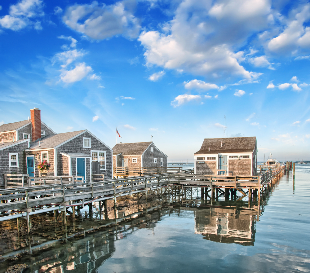 Classic cedar shingled houses in Nantucket Massachusetts. They sit on the water and it is a sunny day. 