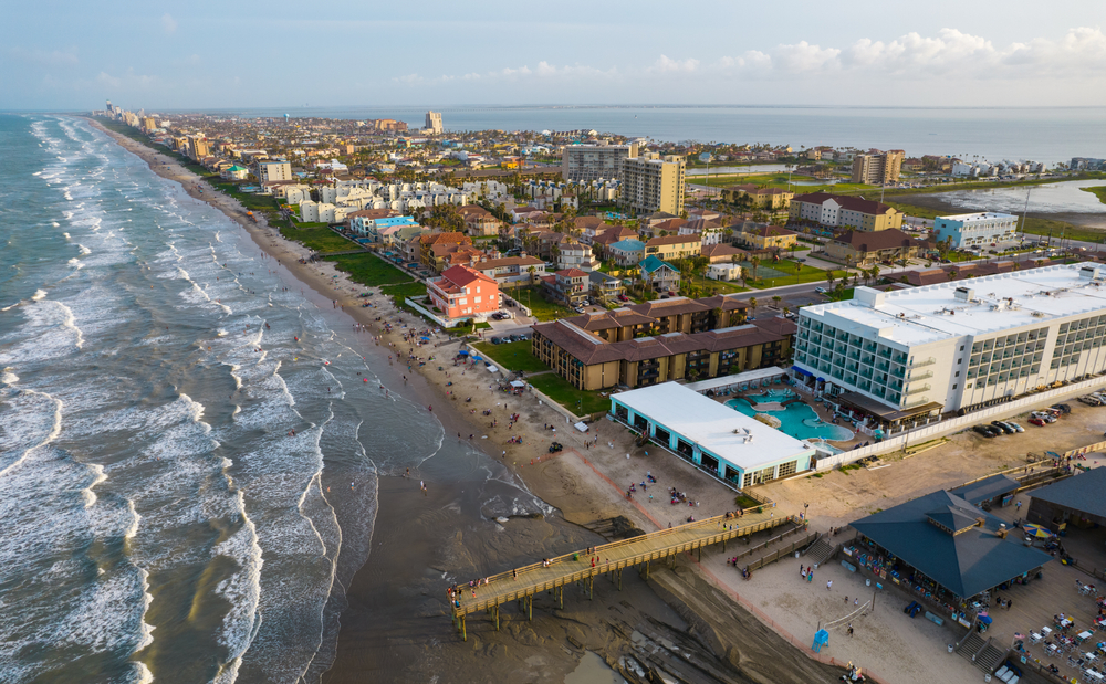 An aerial view of South Padre Island in Texas. It is full of buildings and you can see a pier that leads into the ocean from the shore. 