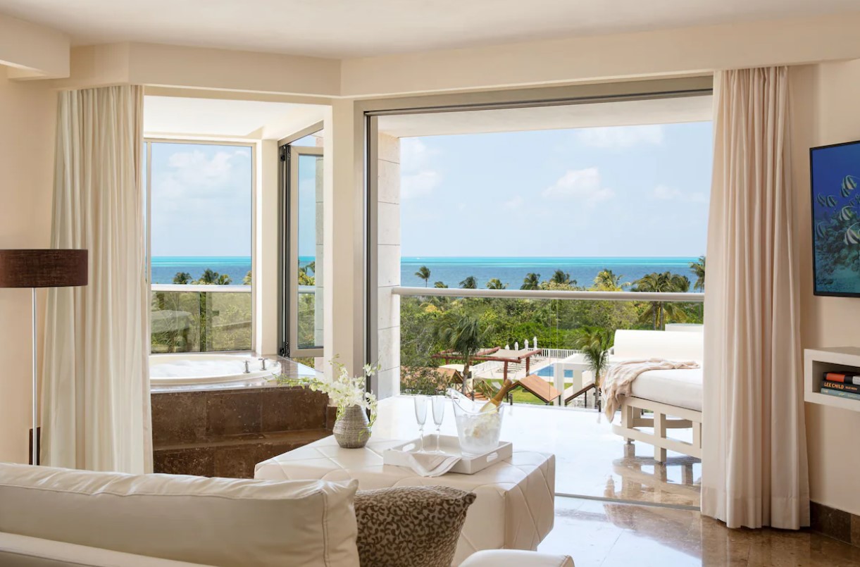 A terrace in a private suite that has views of the ocean, a lounger, and a private hot tub. 