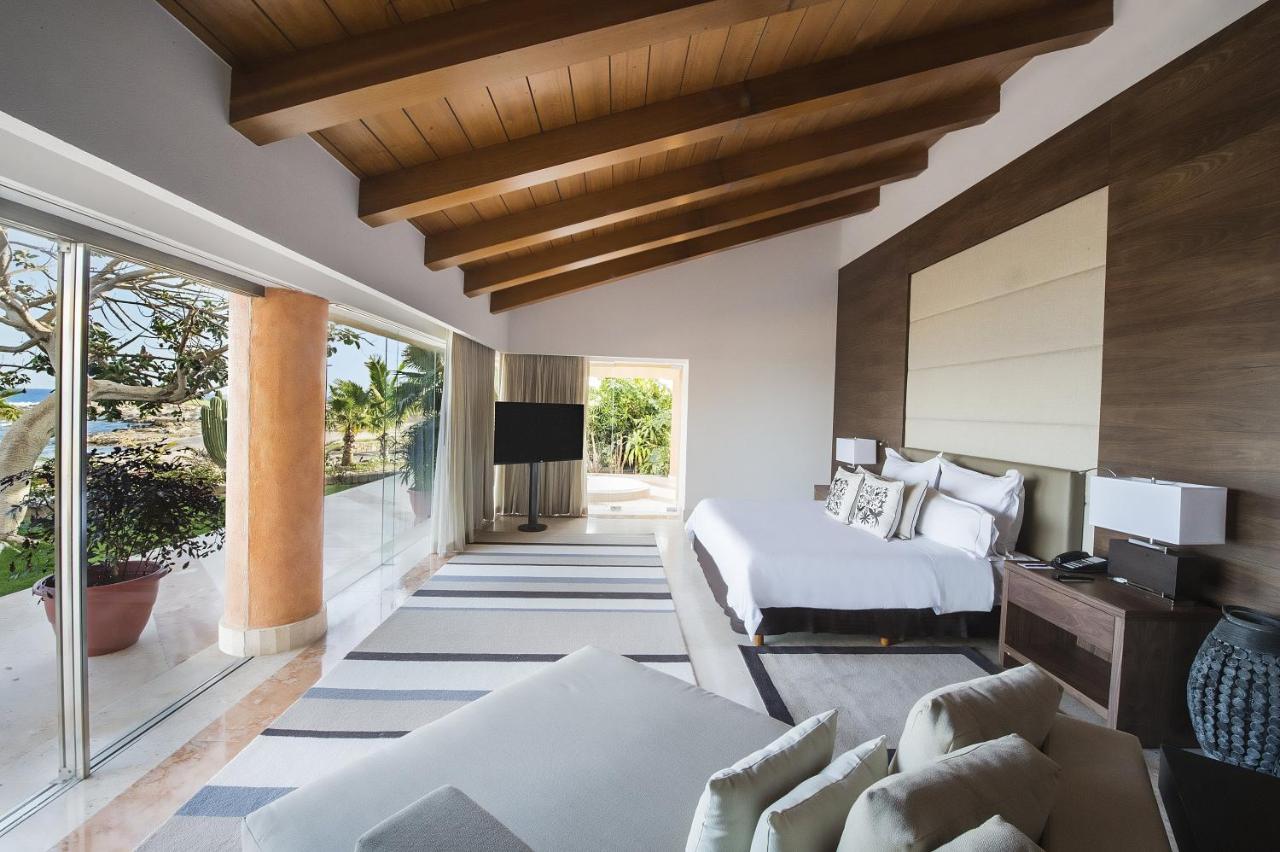 A suite in an all-inclusive resort in Mexico that has a large wall of windows, a king sized bed, and a large lounge chair. 