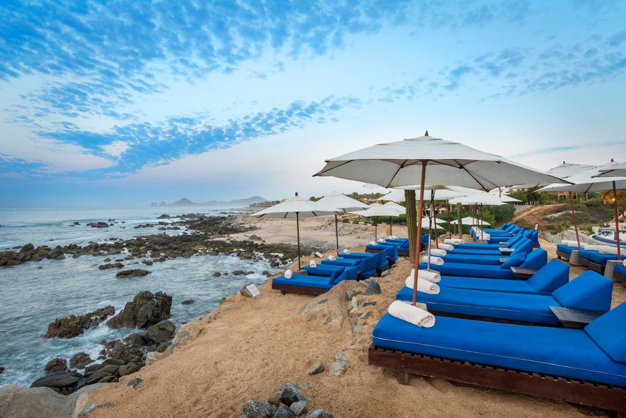 Rows of bright blue beach loungers on the shore of a beach that has some large rocks in Mexico. 