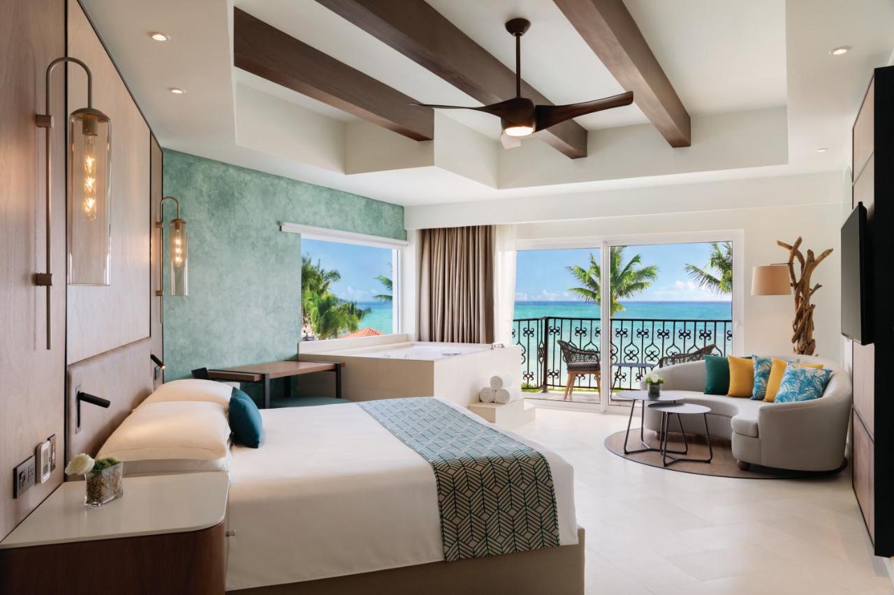 The inside of a suite at an all-inclusive resort in Mexico that has a private hot tub, a large bed, and a terrace that looks out onto the ocean. 