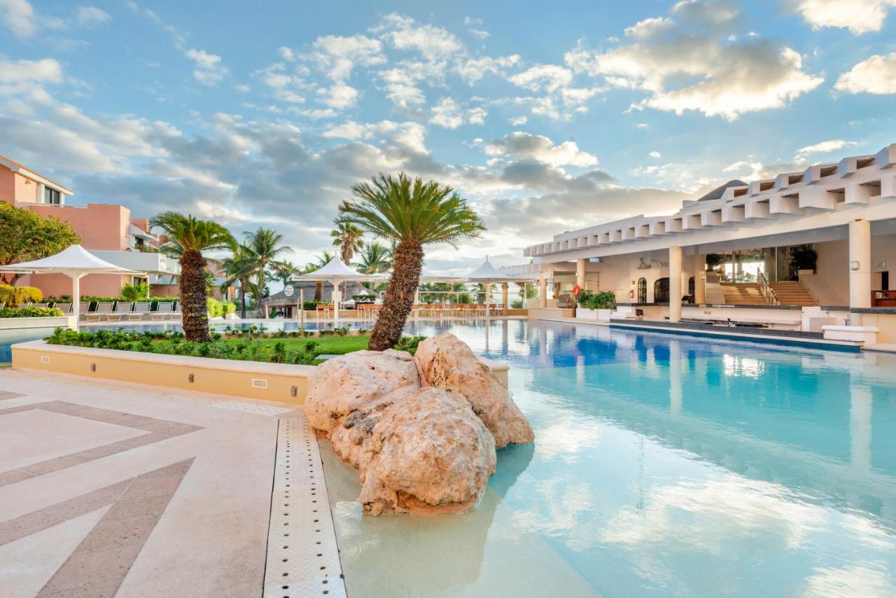 A large pool at an all inclusive resort that has palm trees and is meant to look like the beach. 