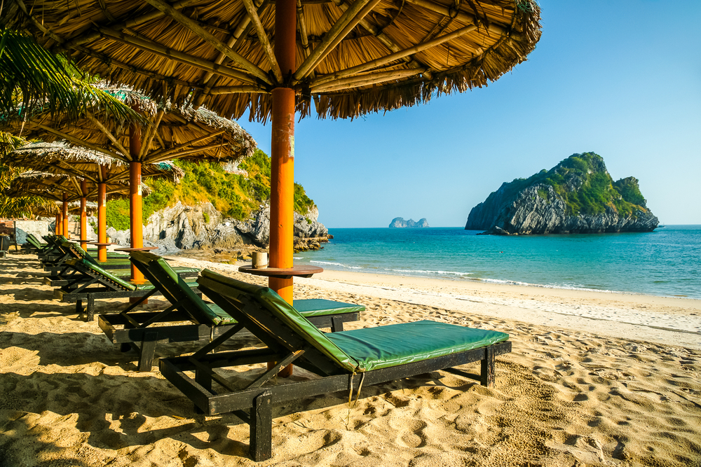 Beach chairs and paraols on the beach with a rocky outcrop in teh sea. 