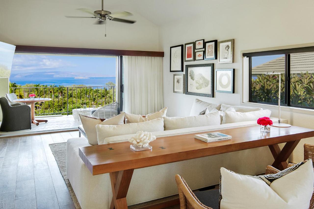 The living area of a suite in a luxury hotel. It has white couches, lots of windows, and a balcony that looks out at the ocean. 