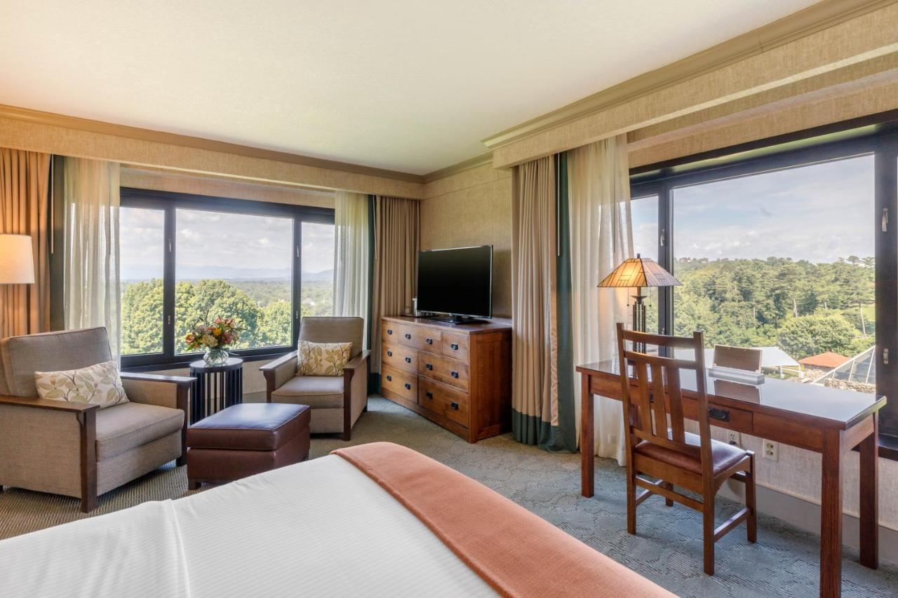 An elegant room with oak furniture, a small sitting area, and large windows on two walls that look out onto the Blue Ridge Mountains. 