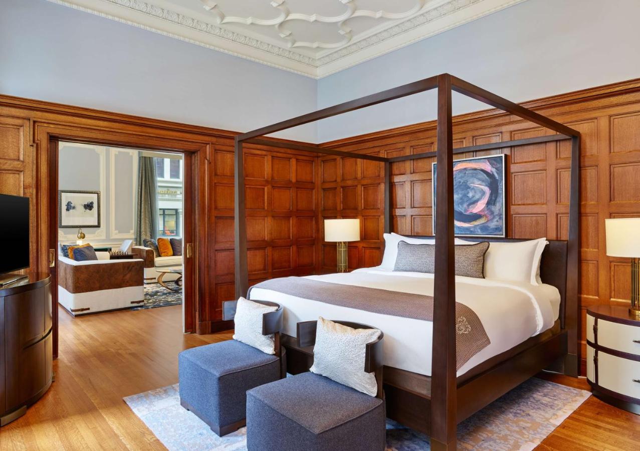 A large four poster bed in a wood paneled room with an ornate ceiling. There is a door that leads to a private sitting area in one of the best luxury hotels in the USA. 