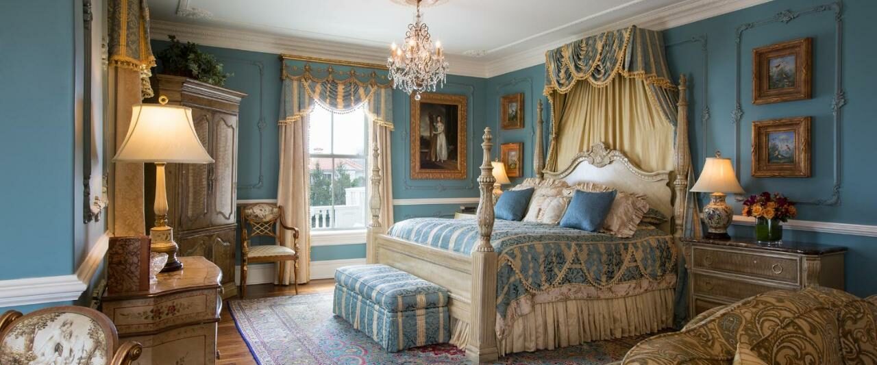 An ornately decorated bedroom with blue walls, an ornate bed, a chandelier, and more. Its a room in one of the best luxury hotels in the USA.