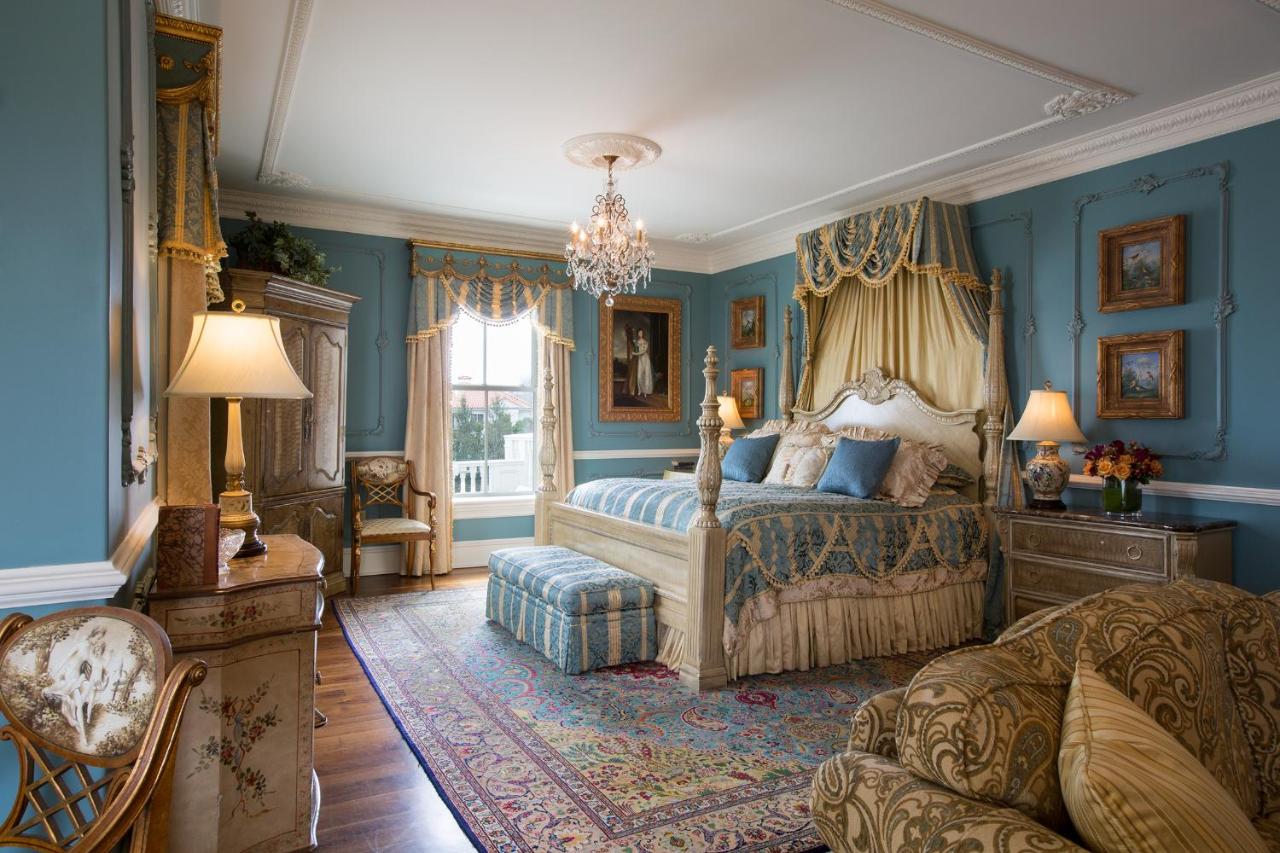 An ornately decorated bedroom with blue walls, an ornate bed, a chandelier, and more. Its a room in one of the best luxury hotels in the USA.