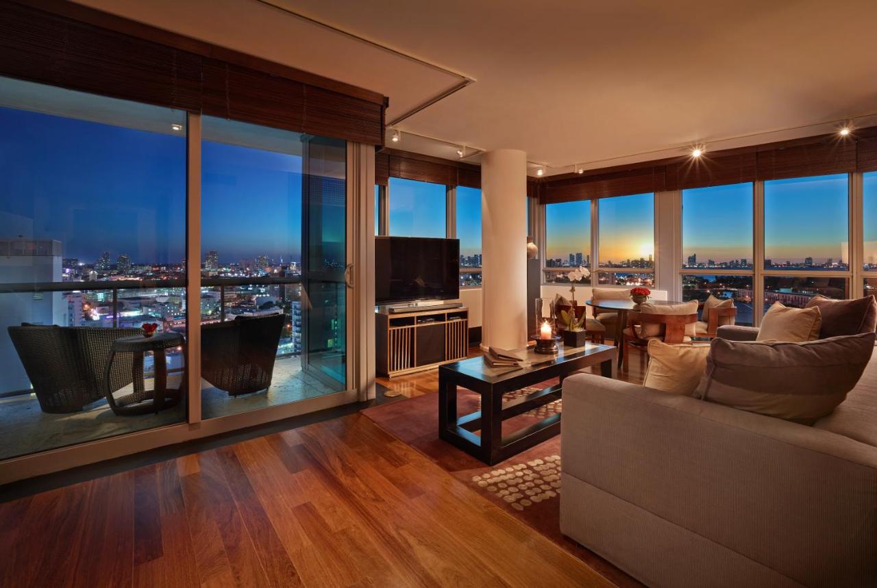 The large living area of a suite in one of the best luxury hotels in the USA. It has walls of windows that look out onto Miami at night. 