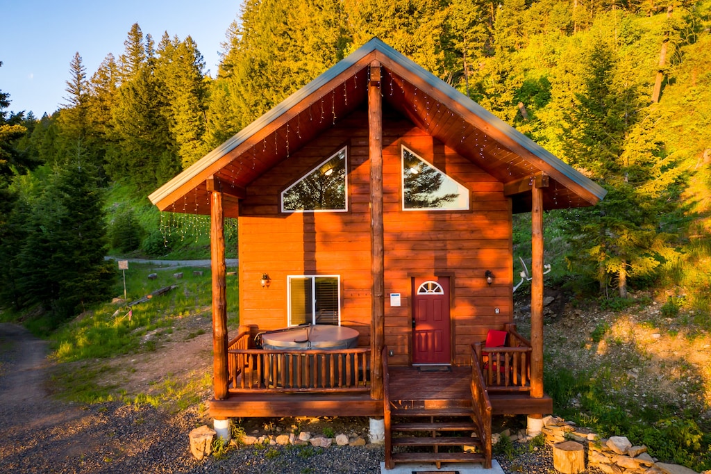 View of a peaked cabin with a front porch containing a round hot tub. 