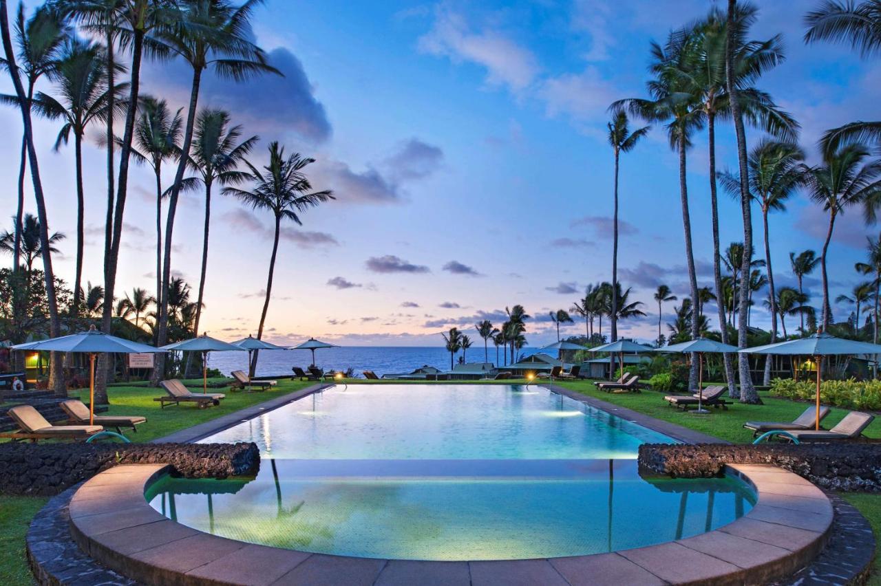 Sunset over the pool and palm trees at Hana-Maui Resort with the ocean in the distance.