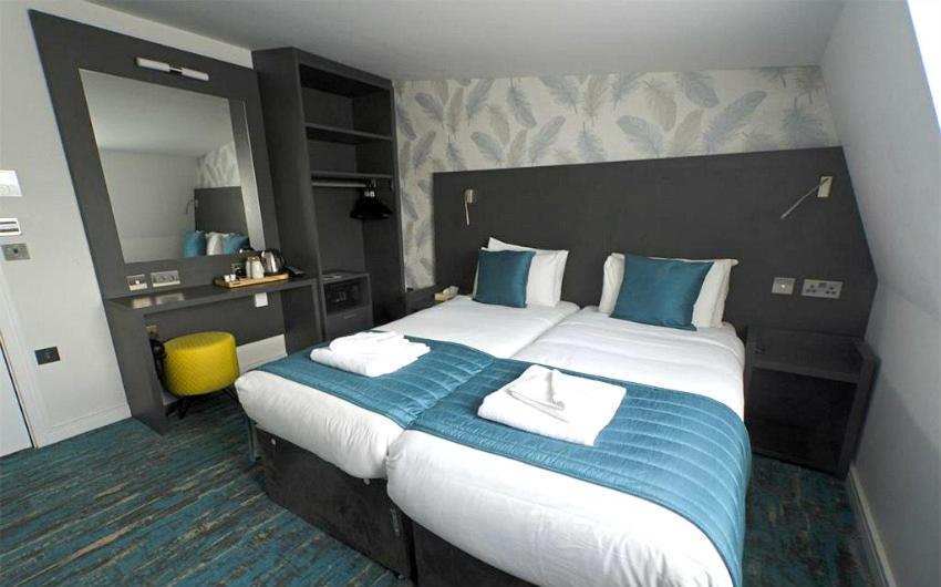 Two twin beds in a room at the K Hotel Kensington with big mirror and lots of storage.