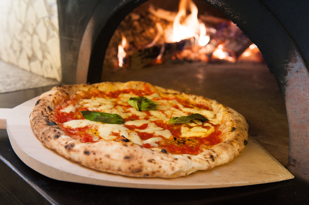 A hand made pizza coming out of a wood burning stove.
