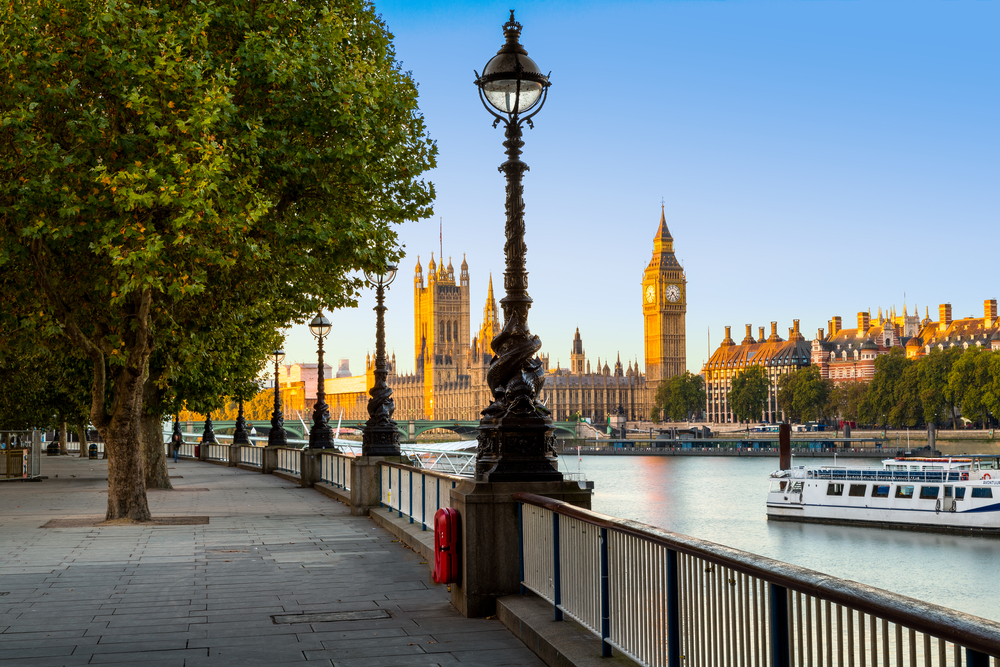 Line of streetlamps overlook the River Thames with Big Ben and the Parliament building in the distance.